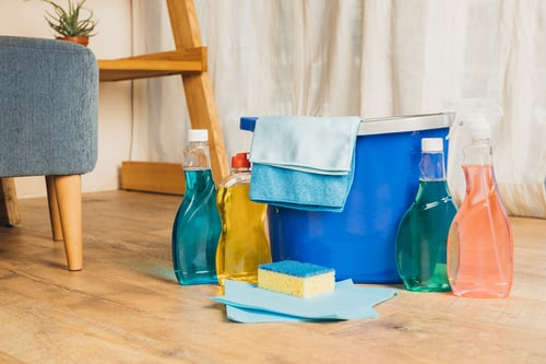 Blue cleaning bucket, cloths, and spray bottles on a wooden floor